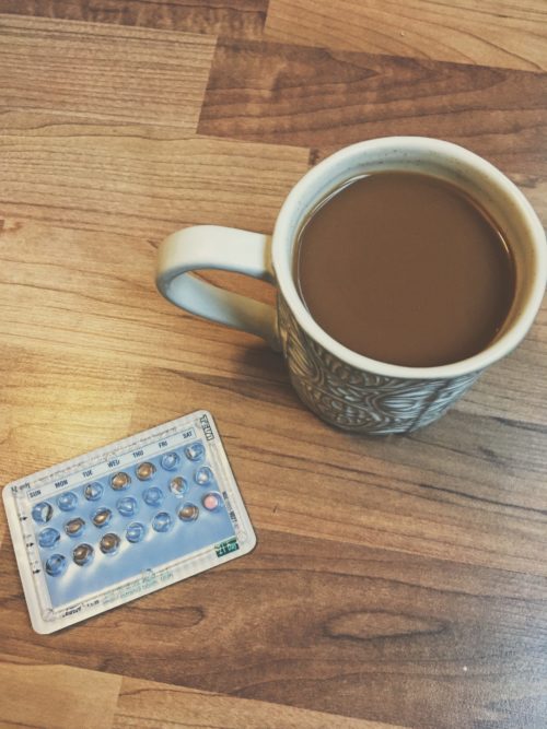 cup of coffee and pack of birth control pills on wood table