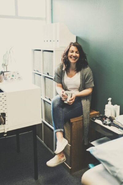 Woman, Dr. Amanda Davis, sitting in physical therapy office drinking coffee