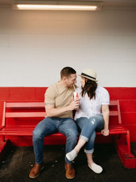 Man and women sitting on red bench sharing a soda