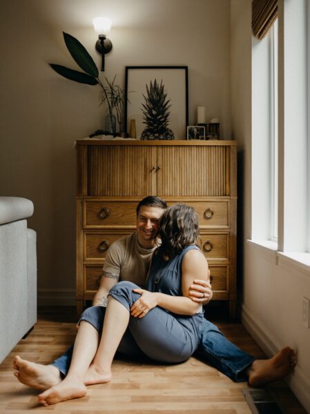 Man and woman kissing while sitting on the floor in front of wood furniture