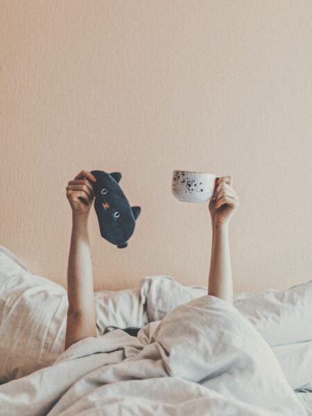 Arms in bed holding coffee and face mask