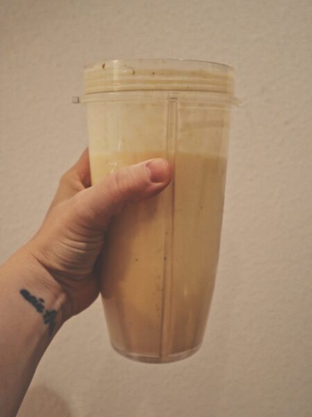 Hand holding an orange smoothie against a white background